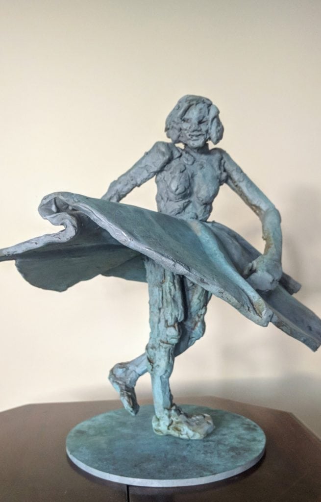 Bronze sculpture of a young girl holding a surfboard, capturing dynamic motion and youthful energy, created by artist Richard Comparey to evoke a sense of playfulness and summer seaside vibes.