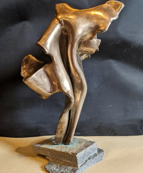 A modern abstract bronze sculpture of a female figure with flowing contours, mounted on a textured stone base.